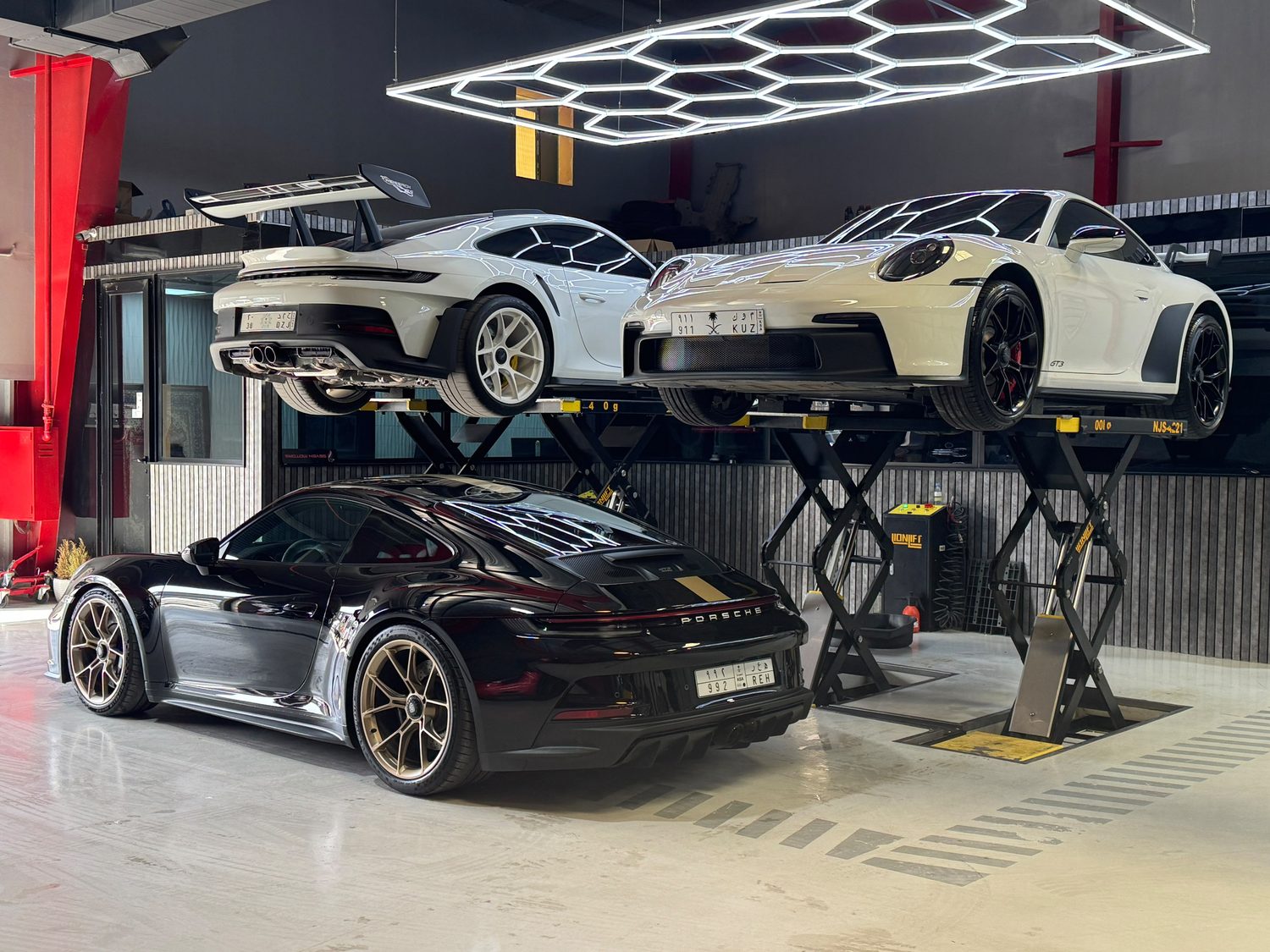 Two Porsche 911 GT3s raised on scissor lifts beside a 992 S/T